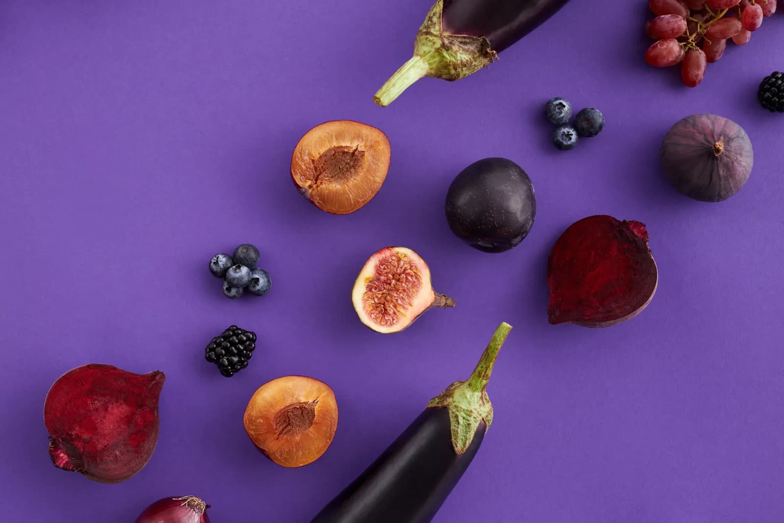 Higos, betabel, berenjena, uvas y moras sobre fondo morado